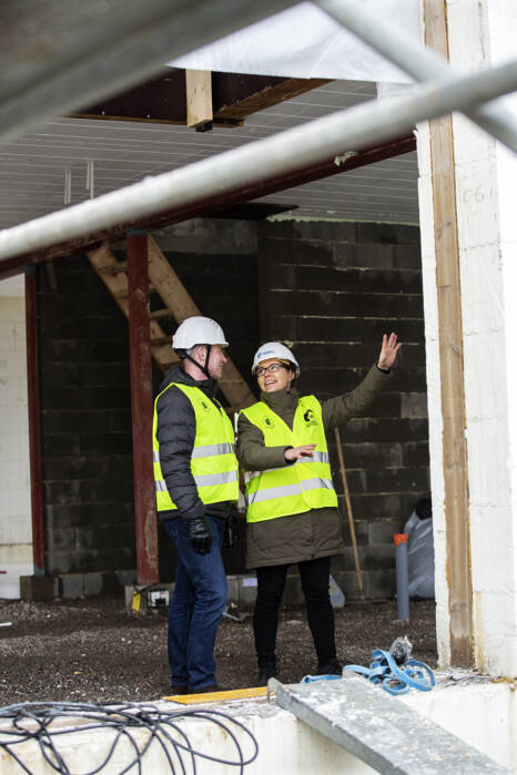 Two construction professionals in safety vests and hard hats discussing a project inside a building under construction